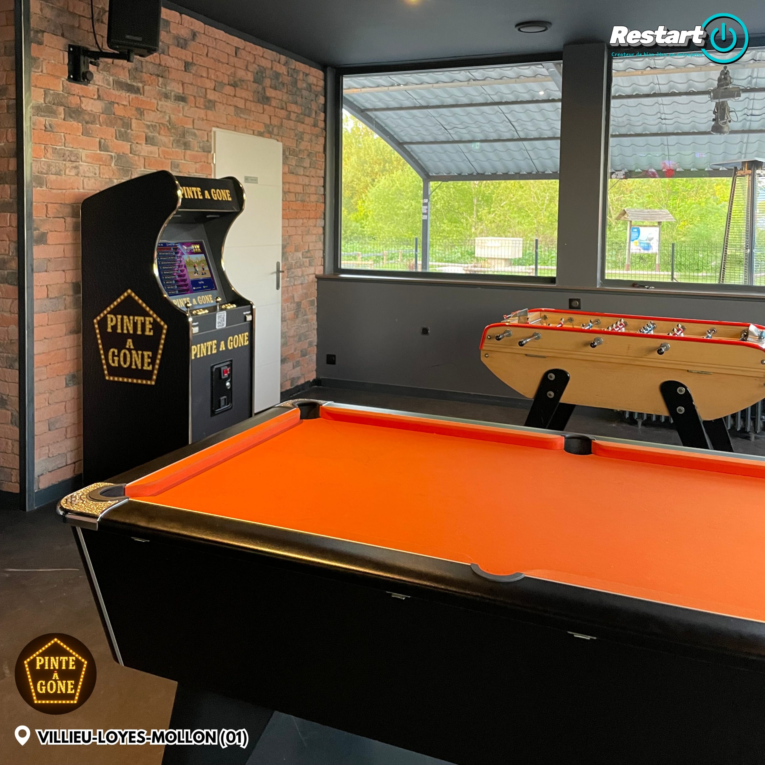 Borne d’arcade personnalisée noire et dorée installée dans un espace de jeux avec un baby-foot et un billard