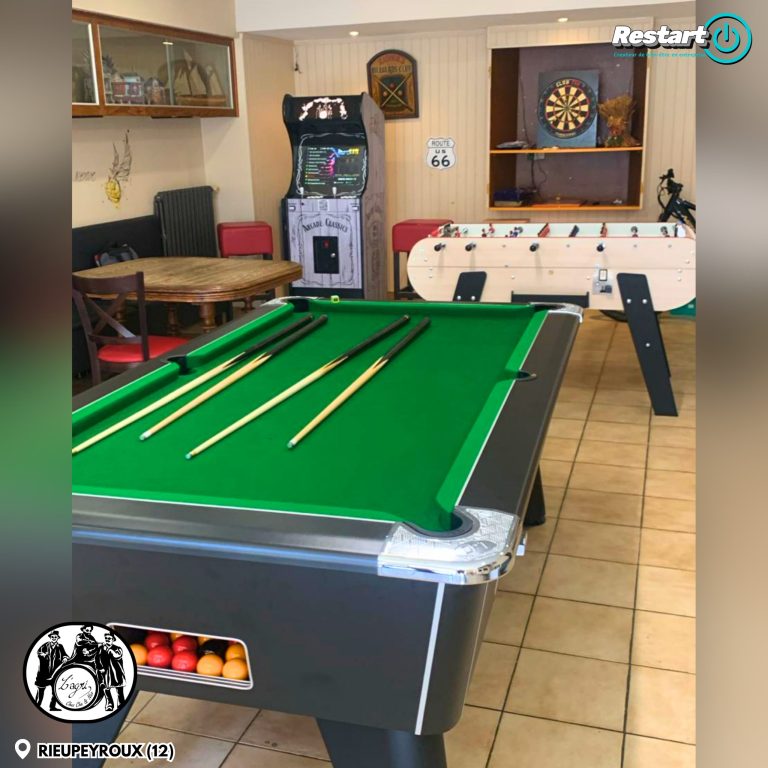 Espace de jeux du Café de l’Agriculture à Rieupeyroux avec billard, baby-foot, cible de fléchettes et borne d’arcade en arrière-plan