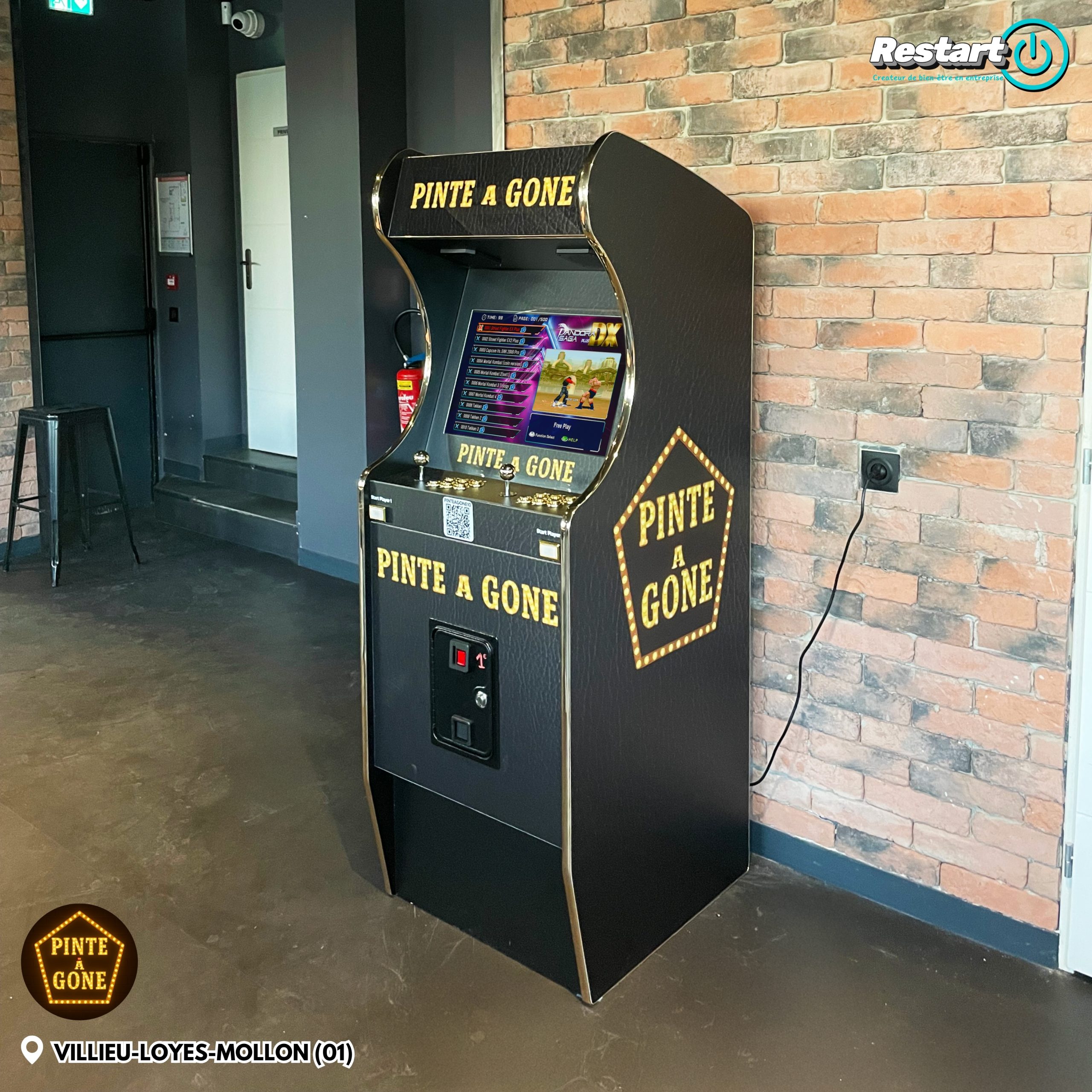 Borne d’arcade personnalisée noire et dorée installée dans un bar devant un mur en briques