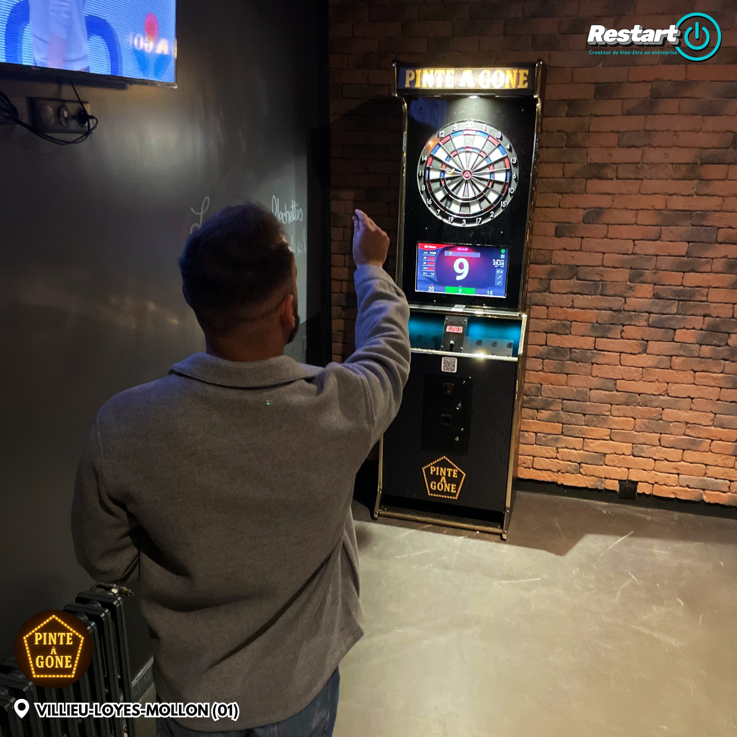 Client jouant sur une borne de fléchettes interactive noire et dorée dans un bar